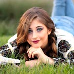Fashionable young woman with braided hair lying on grass, showcasing a vibrant look.