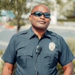 Portrait of a smiling police officer in sunglasses and uniform outdoors, exuding confidence and professionalism.